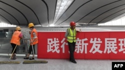 资料照：北京大兴国际机场的工人在一幅“践行新发展理论”的标语旁工作。（2019年7月9日）