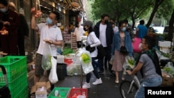 2022年4月25日，新冠肺炎疫情爆发后，戴着防护口罩的人们在商店外的摊位上购买蔬菜。