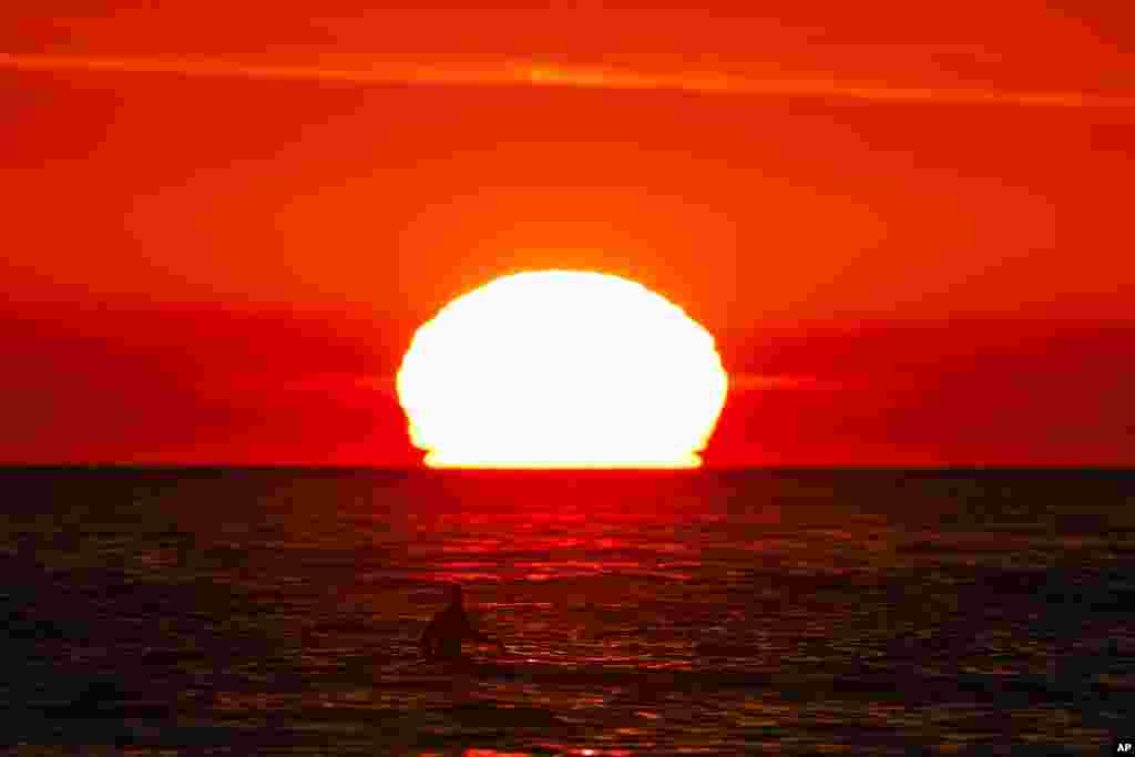 A surfer waits for a wave as the sun sets over the horizon in Pacific Palisades, California.