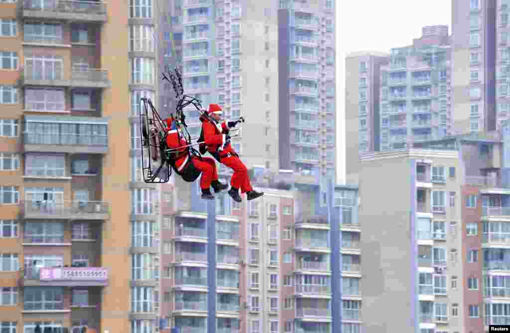 2014年12月24日,贵州省贵阳市庆祝圣诞节活动期间,穿着圣诞老人服装的降落伞俱乐部会员飞过住宅楼,向行人送礼物。