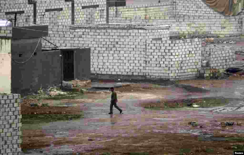 A Syrian man walks in front of his house during heavy rain in the northern Syrian town of Ras al-Ain, as seen from the Turkish border town of Ceylanpinar, Sanliurfa province, November 23, 2012.
