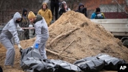 Чоловіки в захисному спорядженні ексгумують тіла мирних жителів, загиблих під час російської окупації в Бучі, на околиці Києва, Україна, середа, 13 квітня 2022 р. Десятки тіл страчених російськими військами вже ексгумовано з братської могили . (AP Photo/Єфрем Лукацький)