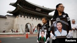 资料照:一名脱北者母亲和她的女儿手持另外一名在逃亡路上去世的脱北者母亲与其儿子的照片,在韩国首尔为母子二人举行葬礼。(2021年9月21日)