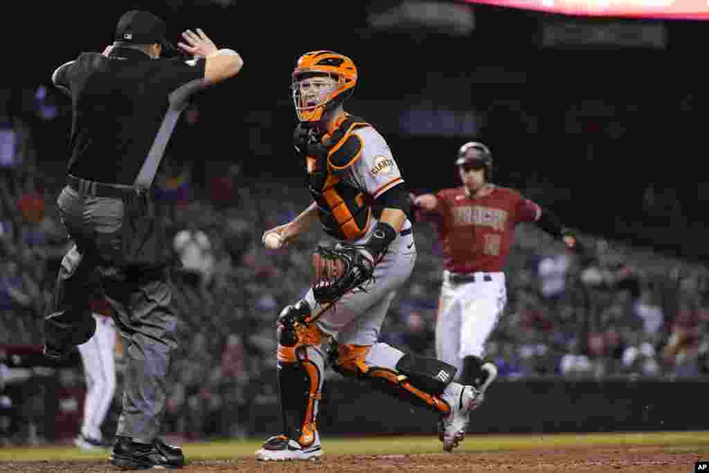 Umpire Nick Mahrley, left, calls a foul ball as San Francisco Giants catcher Buster Posey, middle, questions the call as Arizona Diamondbacks&#39; Tim Locastro, right, runs toward home plate during the ninth inning of a baseball game in Phoenix, Arizona, May 26, 2021.