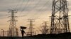 FILE - A woman carries firewood on her head as she walks below Eskom's electricity pylons in Soweto, South Africa, Aug. 8, 2016.