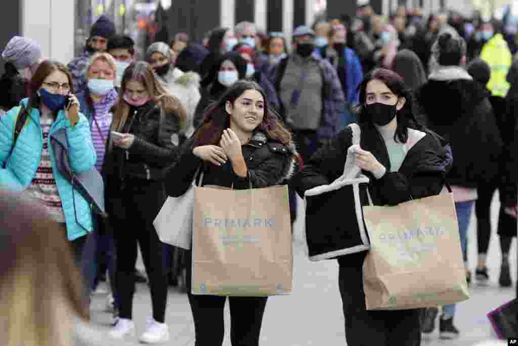 People carry shopping bags while others queue to enter a store on Oxford Street in London. Millions of people will get their first chance in months for haircuts, casual shopping and restaurant meals, as the government takes the next step on its lockdown-lifting road map.