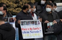安全人员围住在中国驻安卡拉大使馆外举着失联亲人照片抗议的几十名维吾尔人。(2021年2月9日)