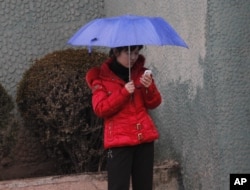 一名朝鲜女性在平壤一条人行道上使用手机。（资料图：2012年3月16日）