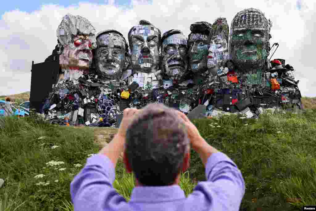 A man photographs "Mount Recyclemore," an artwork depicting the G-7 leaders looking toward Carbis Bay, made from electronic waste by Joe Rush and Alex Wreckage, ahead of the G-7 summit, at Hayle Towans in Cornwall, Britain.
