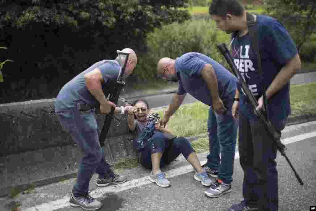 Police officers help a woman who was taking cover against a median barrier during a confrontation between police and suspected drug traffickers along the road known as the Linha Amarela, or Yellow Line, in Rio de Janeiro, Brazil, Jan. 31, 2018.