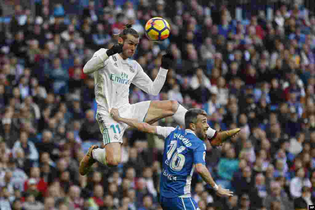 Real Madrid's Gareth Bale, top, outjumps Deportivo Coruna's Luisinho during a Spanish La Liga soccer match between Real Madrid and Deportivo Coruna at the Santiago Bernabeu stadium in Madrid, Spain.