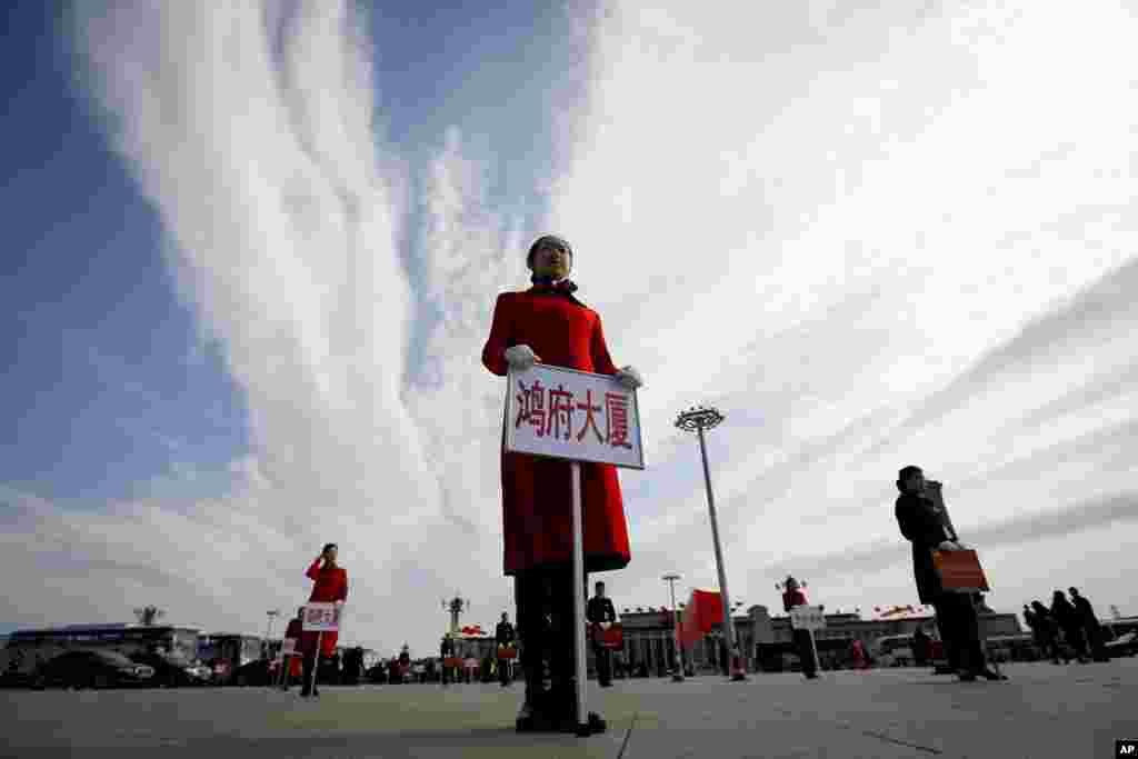 2018年3月15日,中国人民政治协商会议闭幕后,酒店工作人员在人民大会堂外举招牌,通知代表们上车离开。这张照片采取仰拍角度,把人拍得高大上,背景是漫天白云。