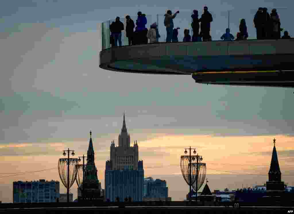 People enjoy the view from a pedestrian bridge in the Zaryadye Park, with the Kremlin's towers and the Russian Foreign Ministry headquarters seen in the background, in Moscow, Russia.