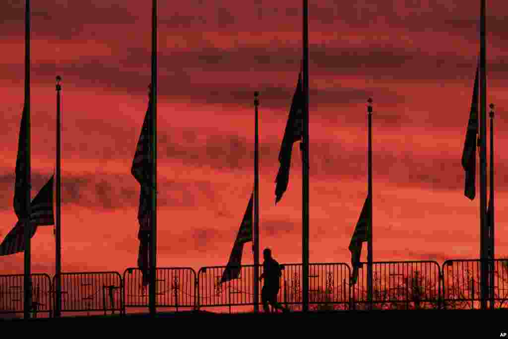 A solitary runner passes under the flags hanging at half-staff surrounding the Washington Monument at day break in Washington, D.C.