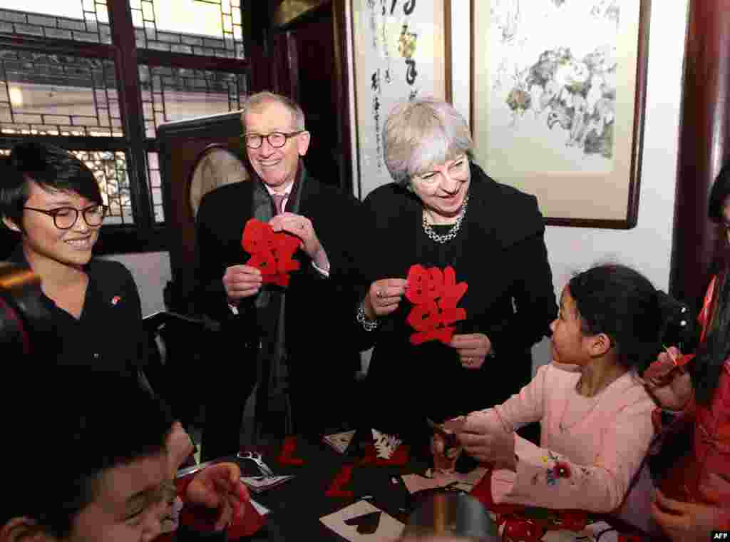2018年2月2日,英国首相特蕾莎·梅(Theresa May)和她的丈夫菲利普·梅在上海豫园观看学生剪纸,手里拿着福字。