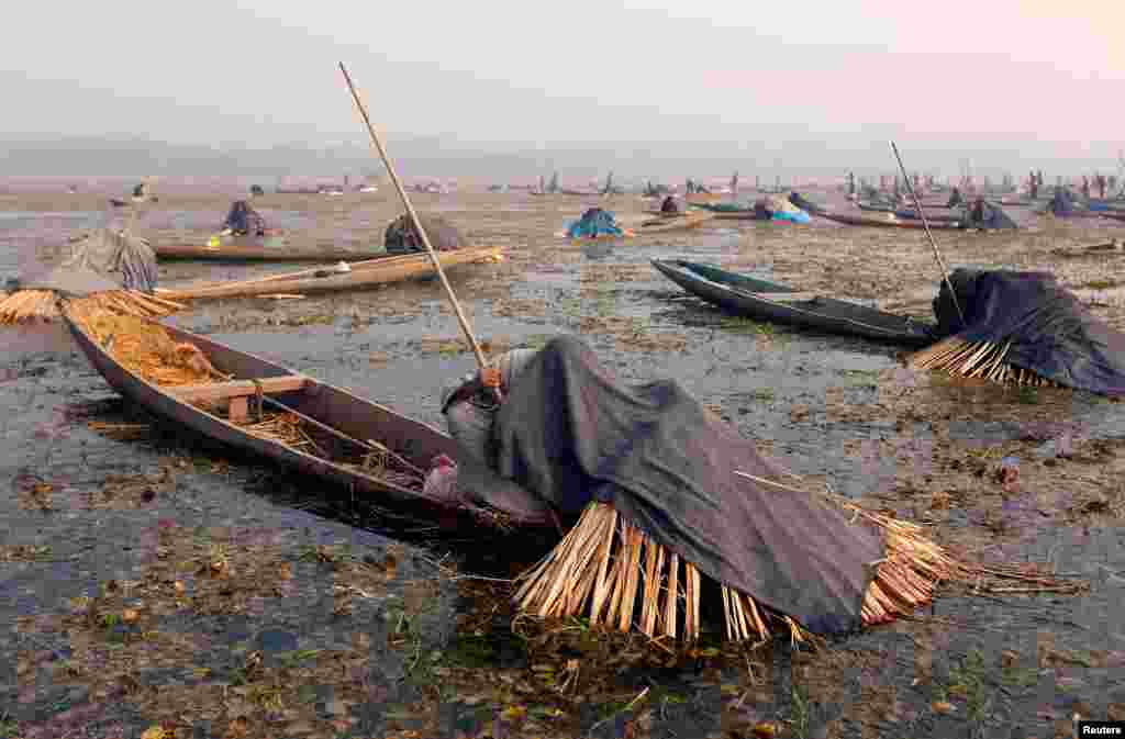 Fishermen cover their heads and part of their boats with blankets and straw as they wait to catch fish in the waters of the Anchar Lake on a cold winter day in Srinagar, India.
