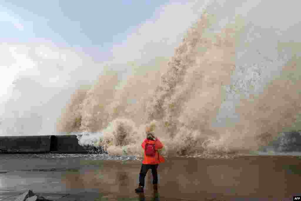 A woman takes photographs as waves crash over the tidal wall along the seafront in New Brighton, north west England.