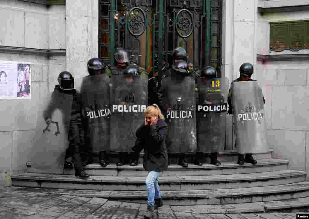 A pedestrian walks in front of riot policemen at the residence of the Bolivian vice president during a protest against the Bolivian government's new health care policies, in La Paz, Jan. 8, 2018.