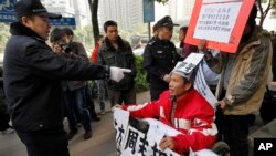在《南方周末》广州总部外，警察指着一名声援《南方周末》的坐轮椅的抗议男子，随后把他带走。（2013年1月10日）