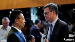 美国驻WTO大使丹尼斯·谢伊(Dennis Shea，又译习达难) (右)在瑞士日内瓦举行的世界贸易组织会议上与中国驻WTO大使张向晨交谈。（2018年7月26日）