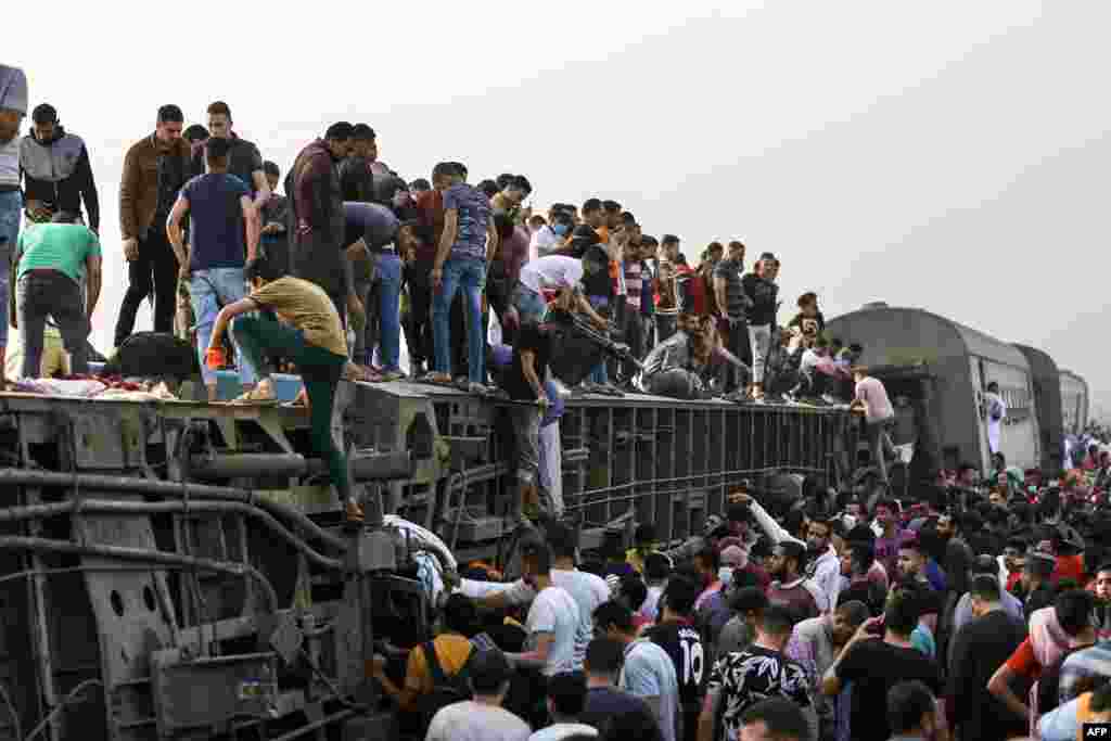 People climb an overturned train carriage as they gather at the scene of a railway accident in the city of Toukh in Egypt's central Nile Delta province of Qalyubiya, April 18, 2021.