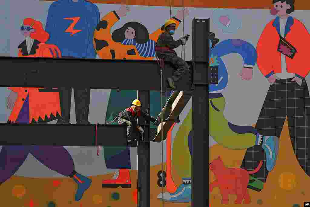 Workers connect metal girders near a wall displaying a fashion scene at the Wangfujing shopping district in Beijing. China's economy maintained stable recovery last month, which is expected to continue, the National Bureau of Statistics announced.