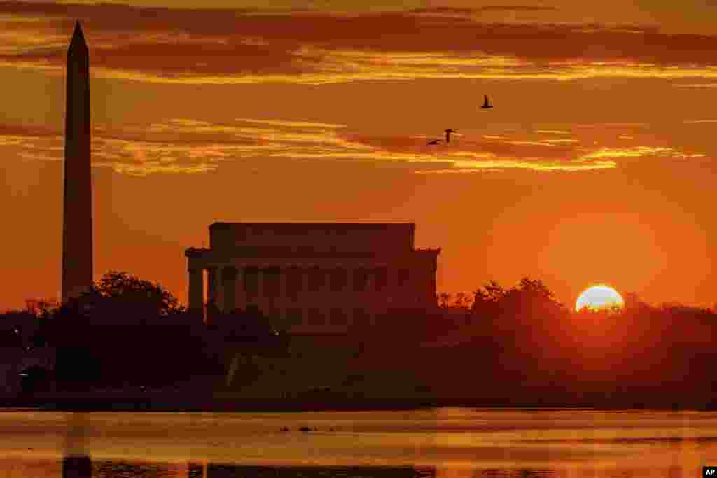 The sun peaks over the horizon next to the Washington Monument and Lincoln Memorial at daybreak along the Potomac River in Washington.