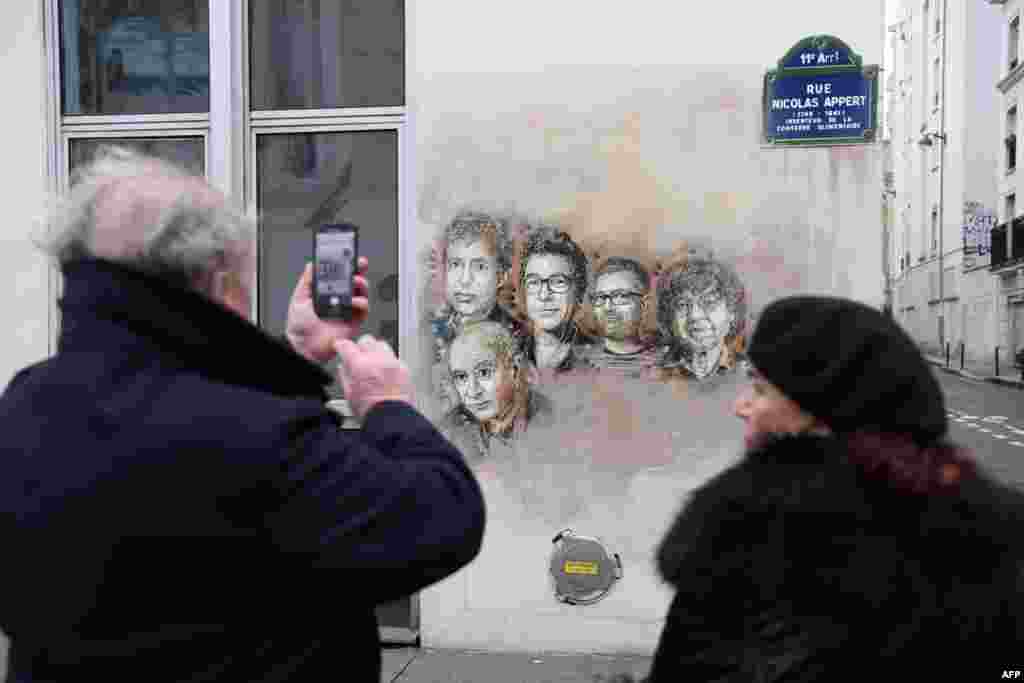 A man takes a picture of portraits (LtoR) of late French satirical weekly Charlie Hebdo's deputy chief editor Bernard Maris, French cartoonists Georges Wolinski, Bernard Verlhac (aka Tignous), Charlie Hebdo editor Stephane Charbonnier (aka Charb) and Jean Cabut (aka Cabu) near the magazine's offices at Rue Nicolas Appert, in Paris on the third anniversary of the jihadist attack on French satirical magazine Charlie Hebdo.