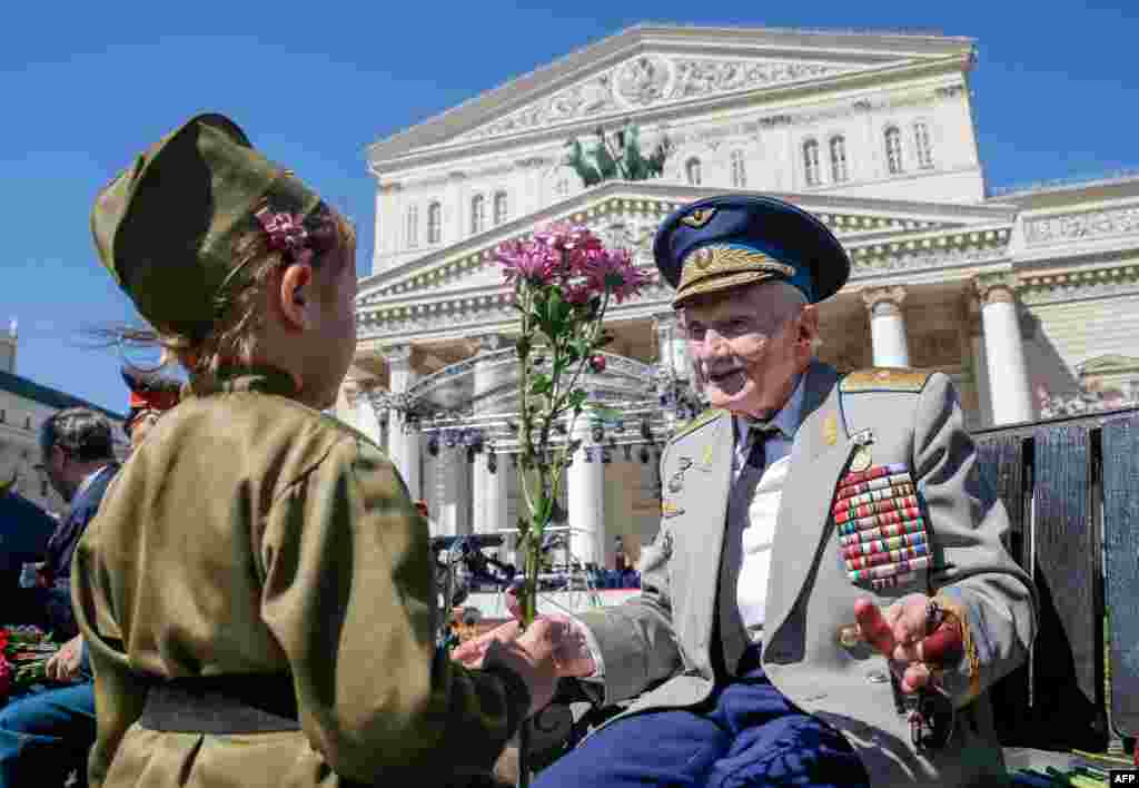 A child presents a flower to a World War II veteran in front the Bolshoi Theatre during Victory Day celebrations in downtown Moscow, Russia.