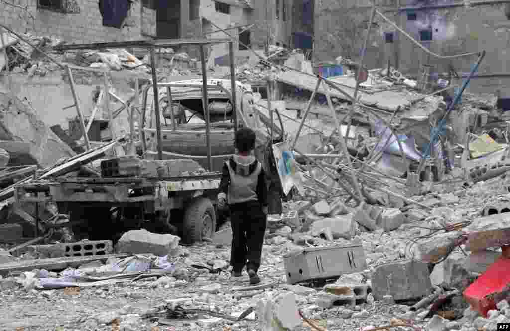 A Syrian boy walks past debris, rubble, and a damaged vehicle in the town of Hazzeh in Eastern Ghouta, on the outskirts of the Syrian capital Damascus.