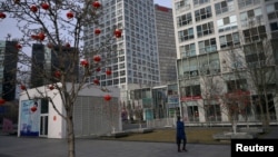 2020年2月18日星期二，只见一位戴口罩的女性在北京市中心商业区一座商业大楼前走过。