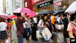 中国游客手提货物，在日本东京银座街道上等待旅游车。（2015年6月17号）