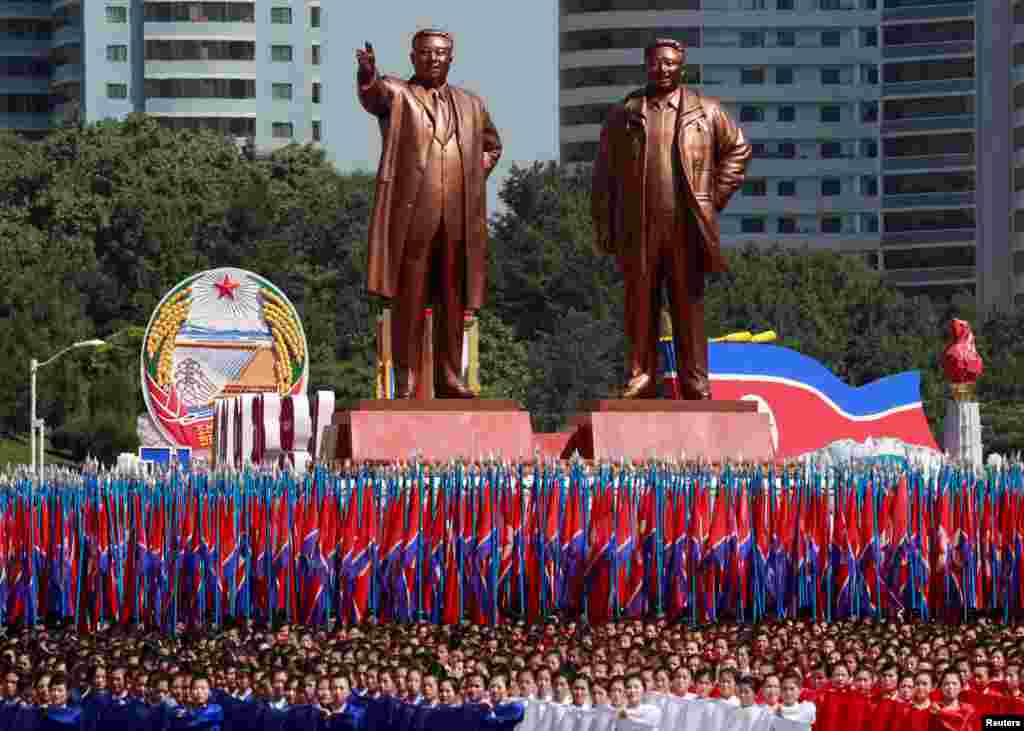 2018年9月9日，朝鲜平壤，在朝鲜成立70周年的阅兵式上，人们携带旗子，在已故朝鲜领导人金日成和金正日的雕像前列队。