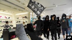 香港黑衣抗议者在铜锣湾的一个商场里举“光复香港，时代革命”的旗子示威。（2019年12月26日）