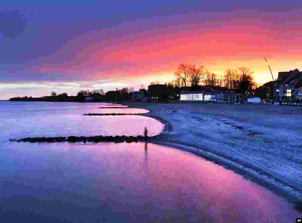 A woman stands at the shore of the Baltic Sea in Niendorf, northern Germany, just before sunrise.