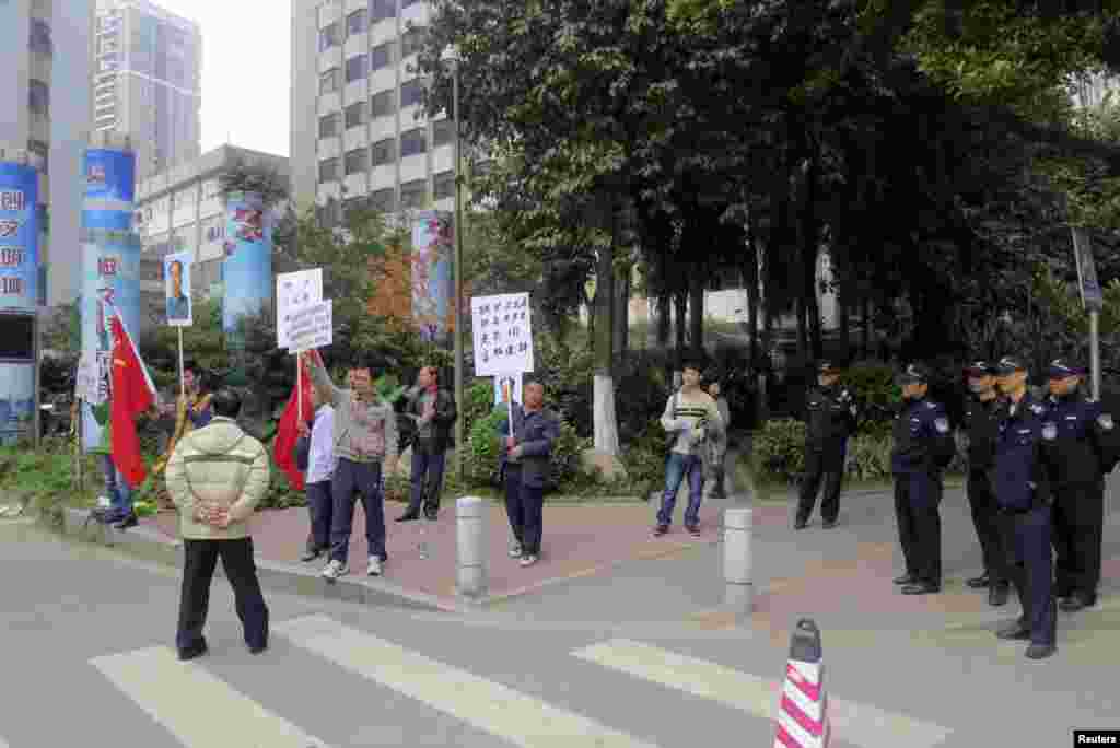 2013年1月8日,示威抗议者在南方周末总部外面的执勤警察旁边举着旗帜和已故毛泽东的遗像