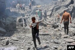 FILE - A boy carries salvaged items from the rubble of a building destroyed during Israeli bombardment at al-Shati refugee camp in Gaza City on June 22, 2024, amid the conflict between Israel and the Palestinian militant group Hamas. (Photo by Omar AL-QA