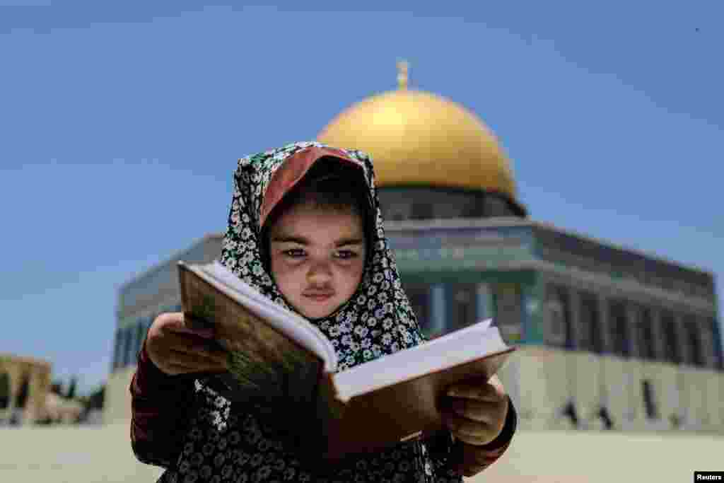 A girl sits with a holy book as the Dome of the Rock is seen in the background at the compound that houses al-Aqsa Mosque, known to Muslims as Noble Sanctuary and to Jews as Temple Mount, in Jerusalem's Old City.