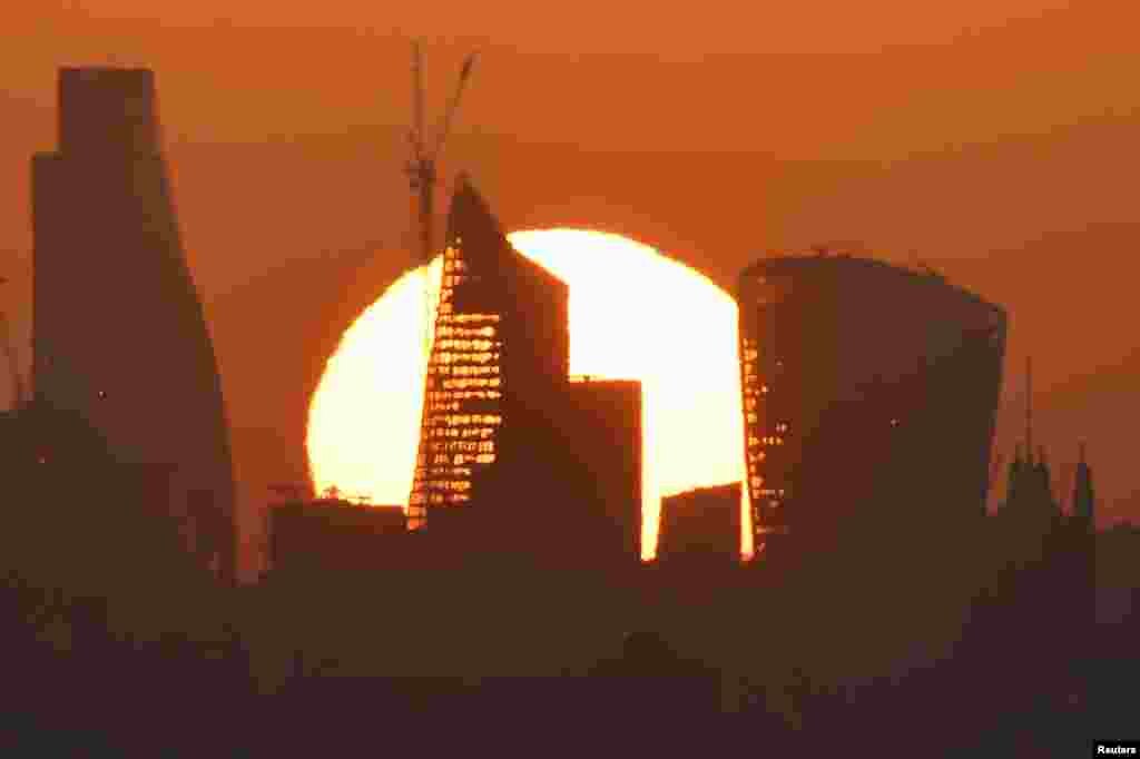 The sun is seen rising over skyscrapers in London's financial district.