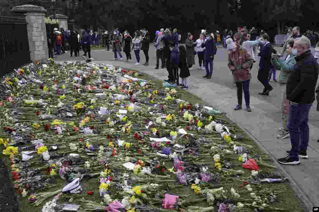 People look at flowers outside Windsor Castle in Windsor, England, to pay tribute to Britain's Prince Philip, the irascible and tough-minded husband of Queen Elizabeth II. 