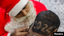 2023年12月31日,在印度艾哈迈达巴德的一家理发店里,一名理发师身穿圣诞老人服装,为客户剪“2024”胡须,迎接新年。(路透社)