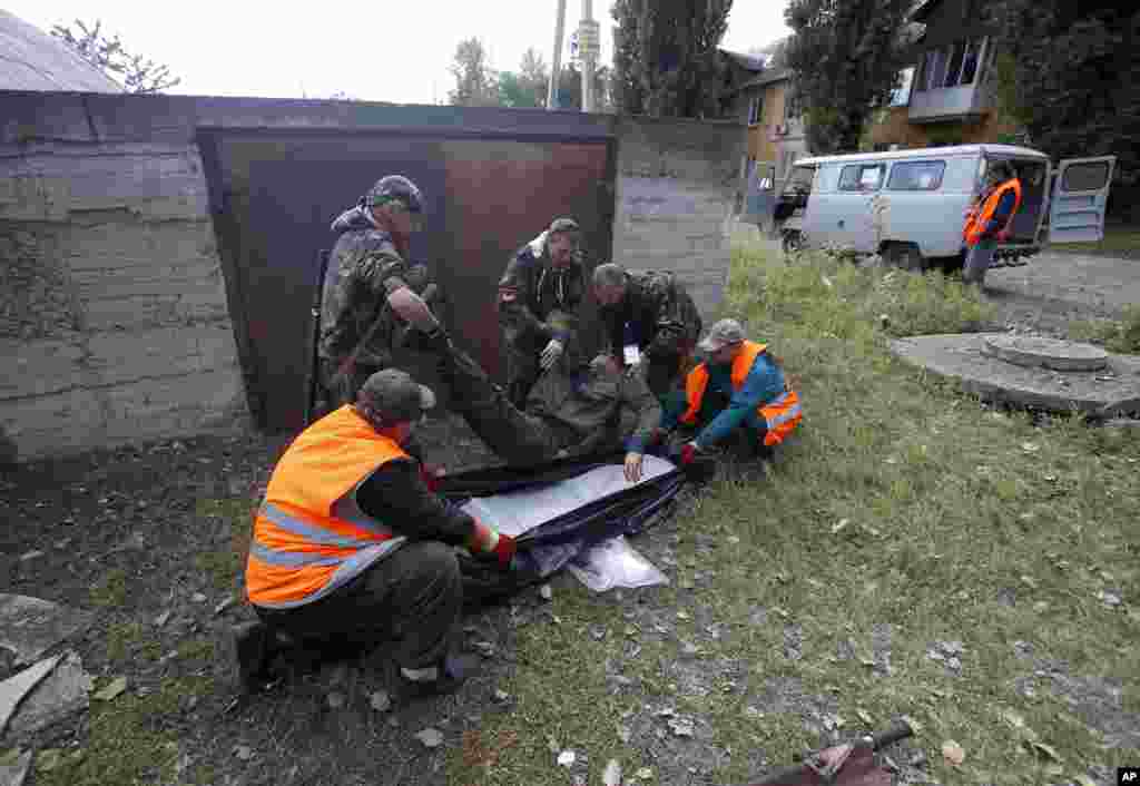 Рятувальники та сепаратисти несуть тіло чоловіка, який загинув під час обстрілу.