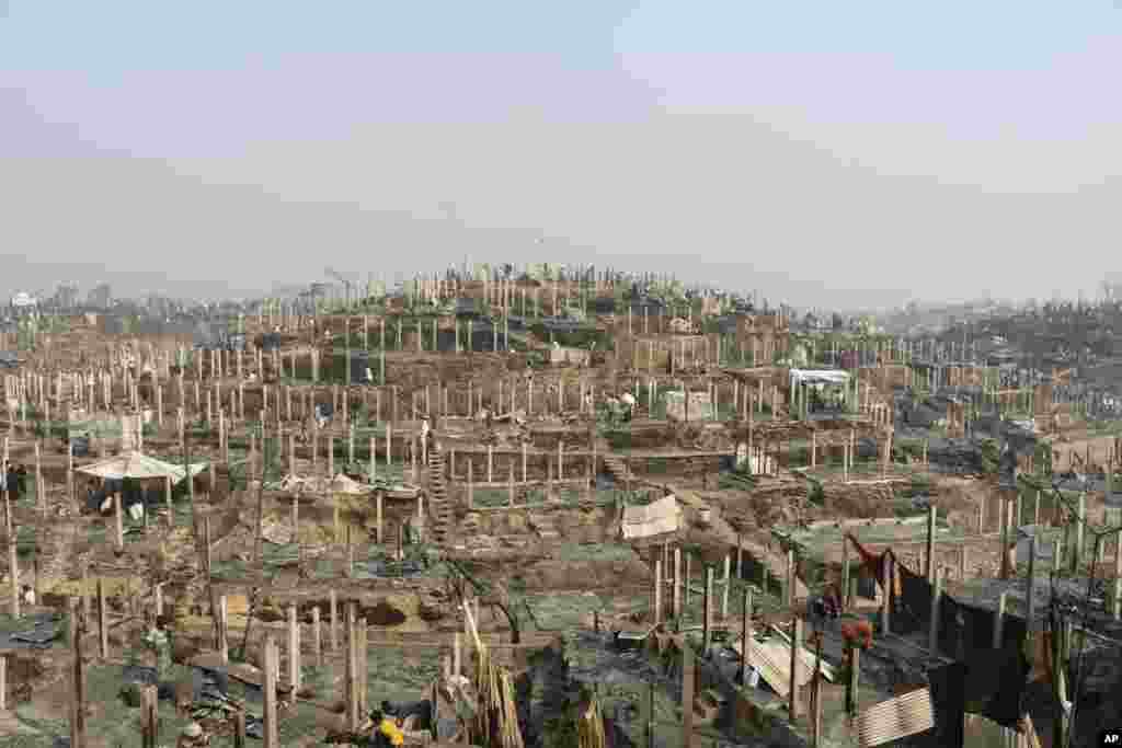 Rohingya refugees stand at the site of Monday's fire at a refugee camp in Balukhali, southern Bangladesh. Rescuers recovered more than a dozen charred bodies from the camp after a devastating fire that destroyed thousands of shelters, officials said. 