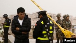 在中国新疆维吾尔自治区喀什的一条街上，警察检查一名男子的身份证，旁边有安全人员（2017年3月24日）