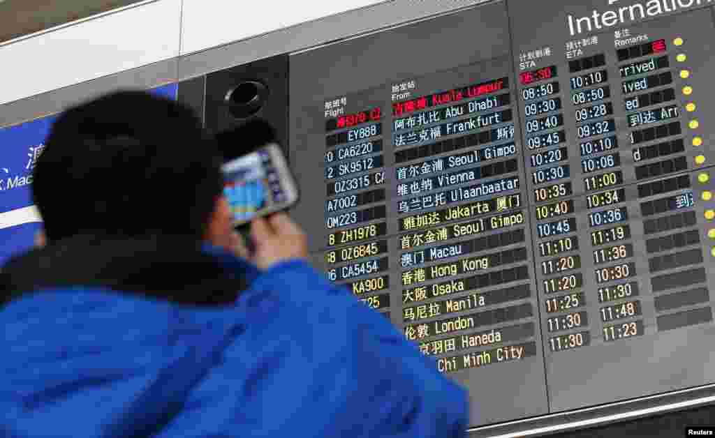 Một người đàn ông chụp hình bảng thông tin chuyến bay với giờ đến của chuyến bay MH370 Malaysia Airlines (hàng đầu, màu đỏ) tại sân bay quốc tế Bắc Kinh, ngày 8/3/2014.