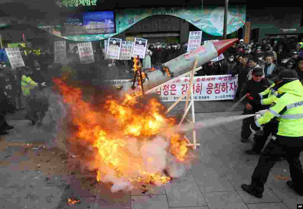 Tại một buổi tụ tập ở Seoul, người biểu tình Nam Triều Tiên đốt một tên lửa giả, khiến cảnh sát phải dùng bình chữa cháy dập tắt. (AP Photo/Ahn Young-joon)
