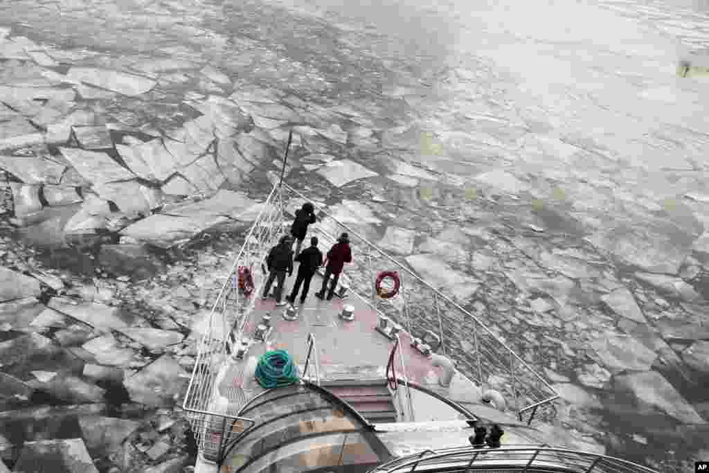 Passengers stand on a deck of a tourist boat specifically designed for winter river cruises as it breaks through the frozen Moskva River in Moscow, Russia.