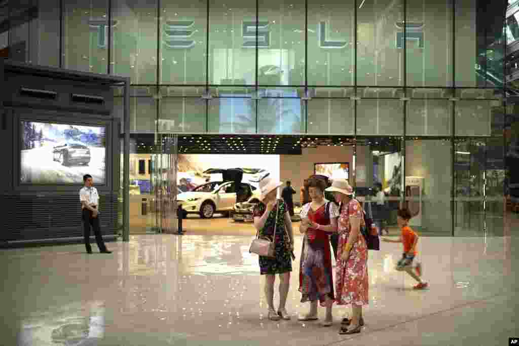 2018年7月5日,一些女士在北京一家高档购物中心的特斯拉展厅外观看智能手机。在美中关税之战中, 中国对包括特斯拉在内的一些美国公司的产品征收25%的关税。为了平衡这次关税增加,特斯拉提升了在中国市场的汽车售价。去年,中国市场上销售的载人电能车辆增加了82%,达到47万辆,是美国同期销售量的两倍。