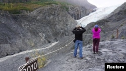 FILE - A sign marks where the end of the Exit Glacier was in 2010 near tourists taking photos in the Kenai Fjords National Park, Alaska, Aug. 31, 2019.