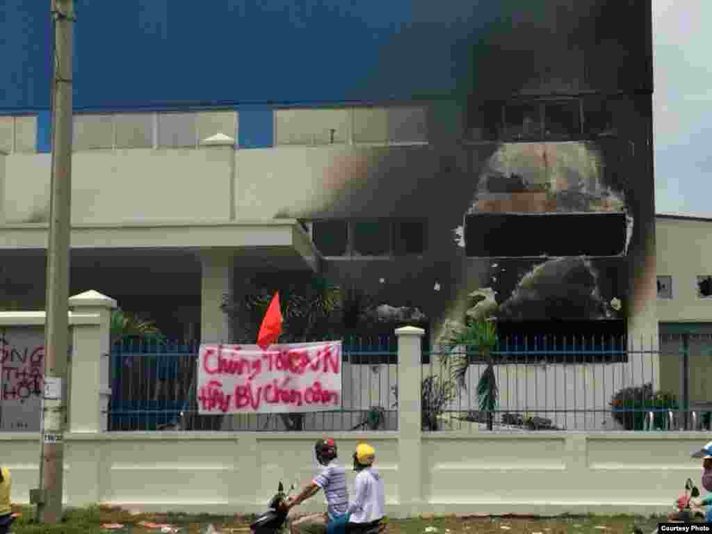 Một nhà máy ở Bình Dương bị đốt. Phía trước là biểu ngữ với hàng chữ 'Chúng tôi yêu Việt Nam. Hãy bảo vệ chén cơm."